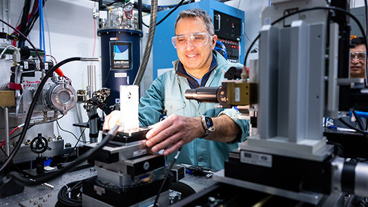 Man wearing safety glasses smiling while working on a machine.
