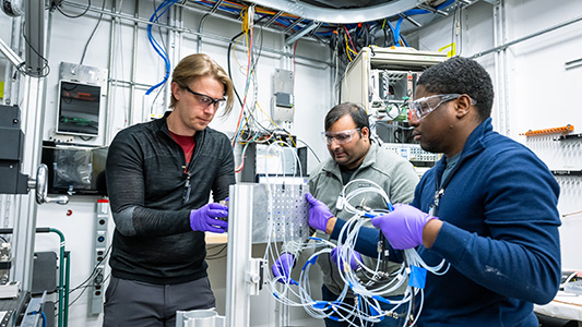 Three men wearing safety glasses holding wires.