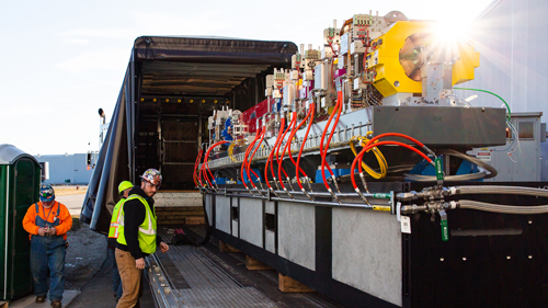 Workers load a large module of magnets onto a truck.