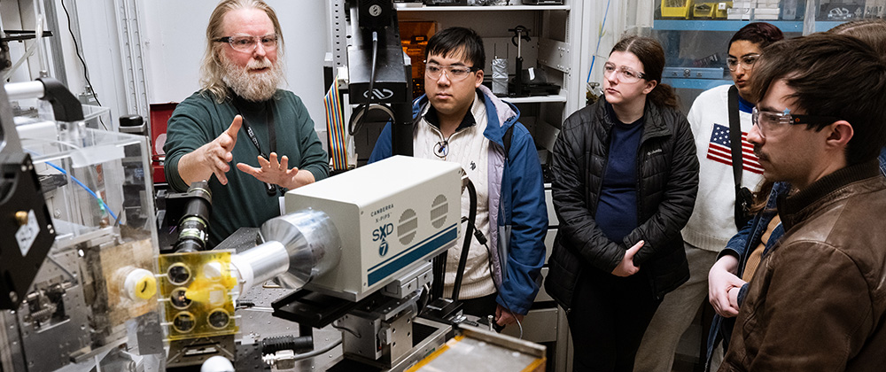 Older man explaining a machine to young adults.