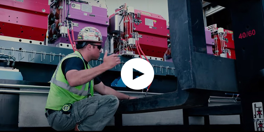 An APS Upgrade worker directs a forklift as it gently lowers a heavy module of colored magnets to the ground.