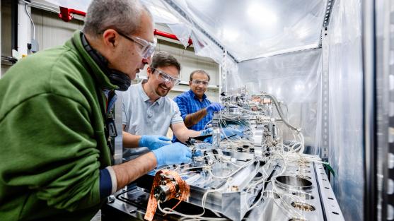 Three men crowd around a piece of technical equipment, working on portions of the device.