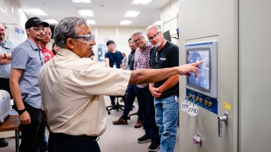 A man presses a button in a control room while his colleagues look on with excitement